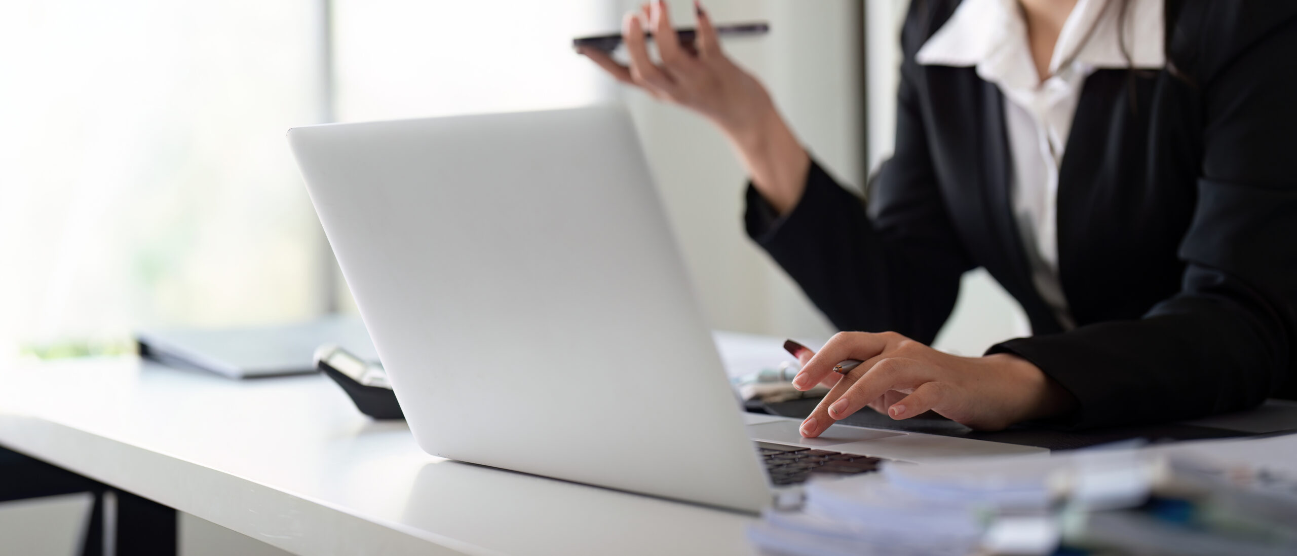 A multitasking female financial professional speaks on the phone while managing data and calculations, demonstrating efficiency in her work.
